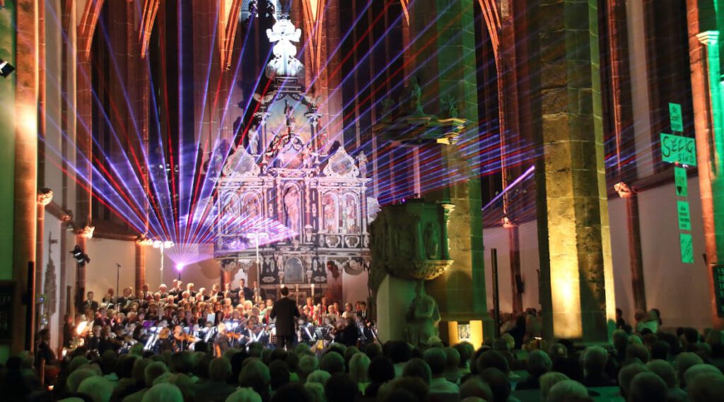 Chorkonzert in einer Kirche mit aufwändiger Veranstaltungstechnik, denn der Innenraum ist bunt und schön ausgeleuchtet.