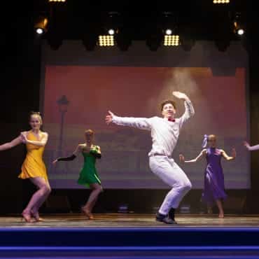 Eine Gruppe Frauen und ein Mann tanzen auf einer Bühne bei einem Musical.